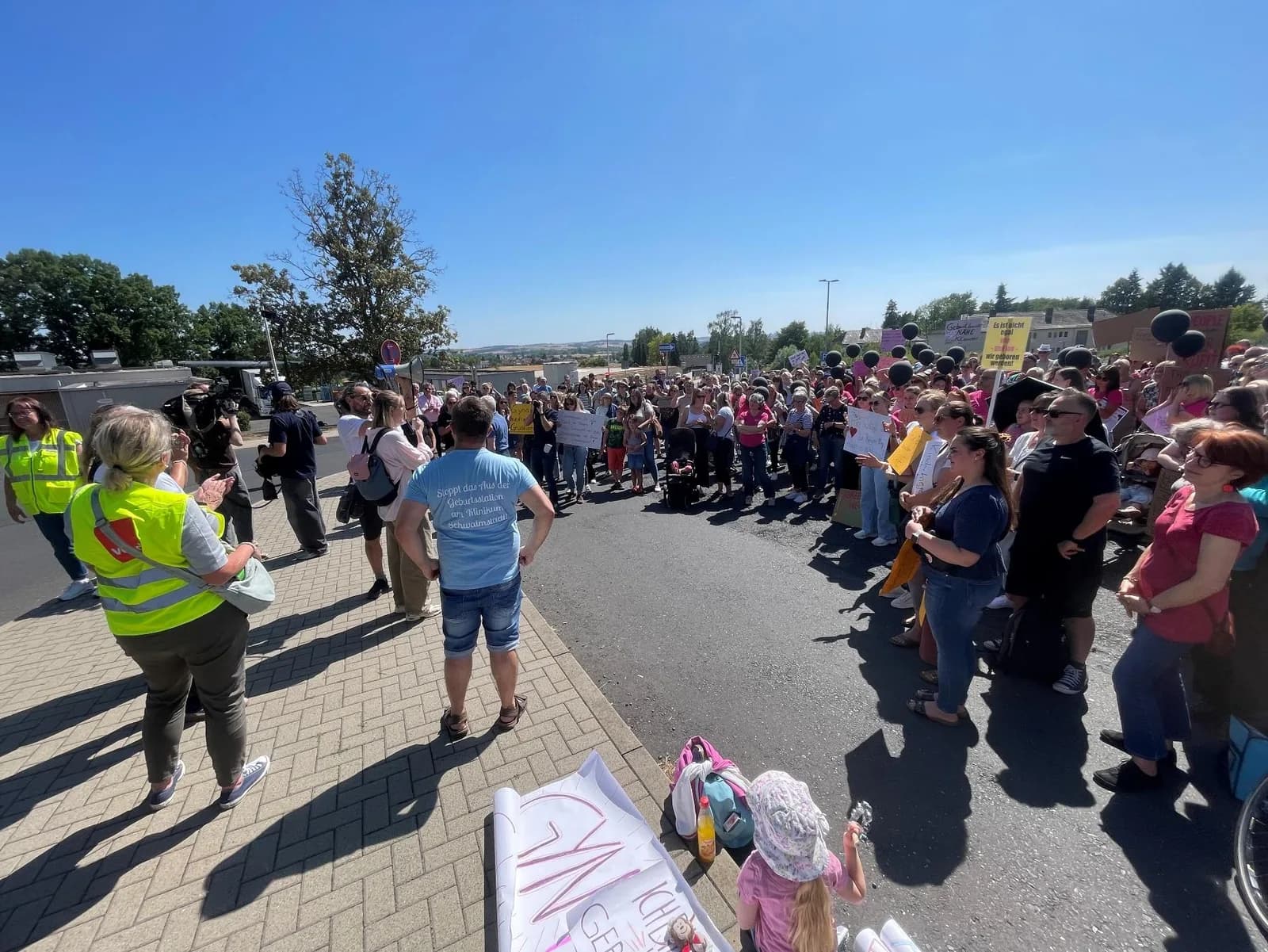 Mehrere hundert Menschen stehen bei Sonnenschein auf dem Parkplatz vor dem Asklepios Klinikum Schwalmstadt.