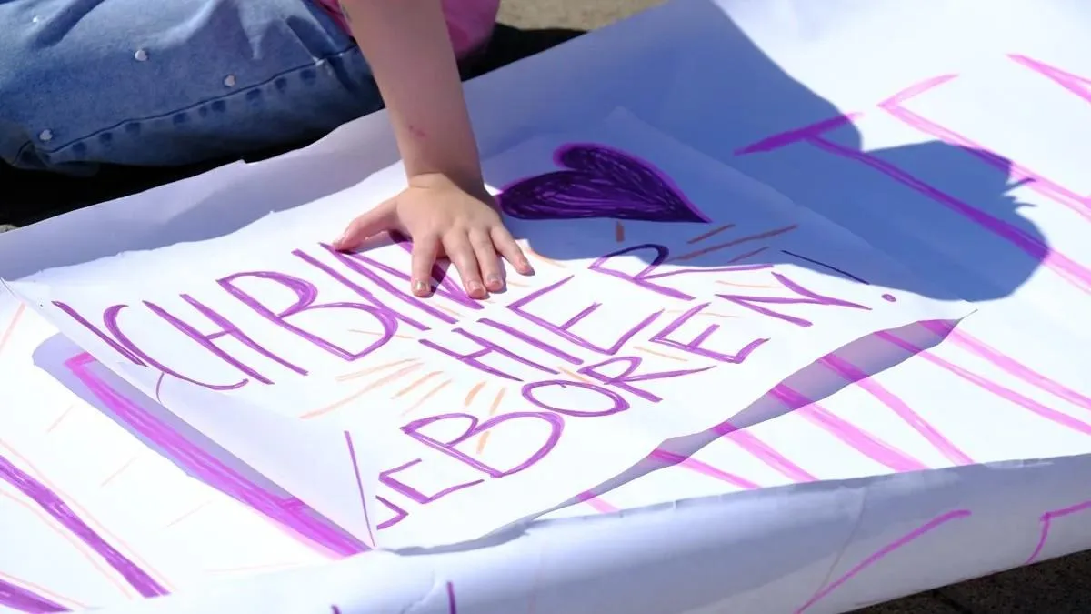 Hände malen mit rosafarbener Farbe den Schriftzug „Ich bin hier geboren“ auf ein Plakat.